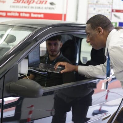 A man leans into a car looking at a laptop through the window.